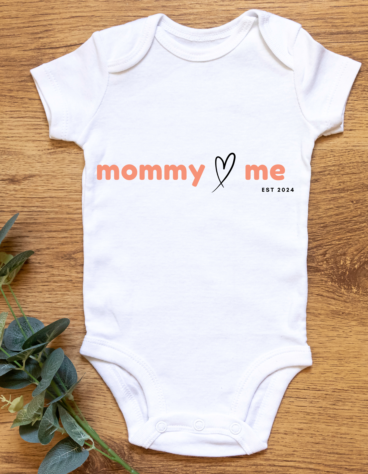 A white onesie with a Mommy heart Me EST 2024 saying.