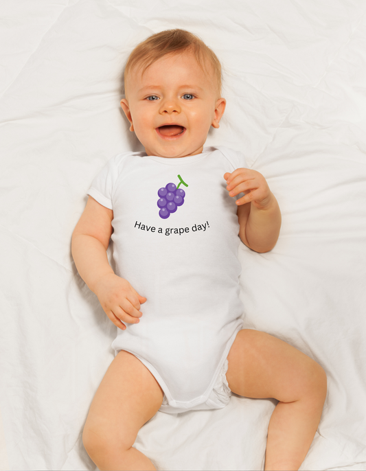 Smiling white baby boy in a white onesie that says have a grape day and has an image of a bunch of grapes.