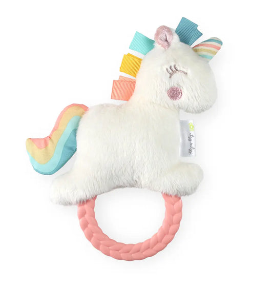image of a rattle that is in the shape of a unicorn that is white with a pink dot for its check, a rubber pink teething ring, and light green, light blue, yellow, and pink fabric tabs as hair with a rainbow horn and tail on a white background