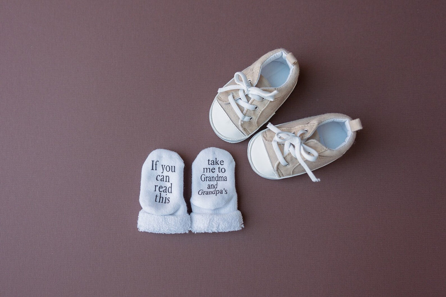 a picture of tan baby shoes and a pair of white baby socks that say if you can read this take me to grandma and grandpas on the sole of the feet on a purple background