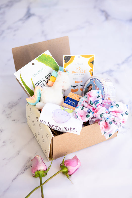 gift box filled with baby products such as face and eye masks, a unicorn rattle, a bow, a onesie, nipple cream, and preggie pop drops 