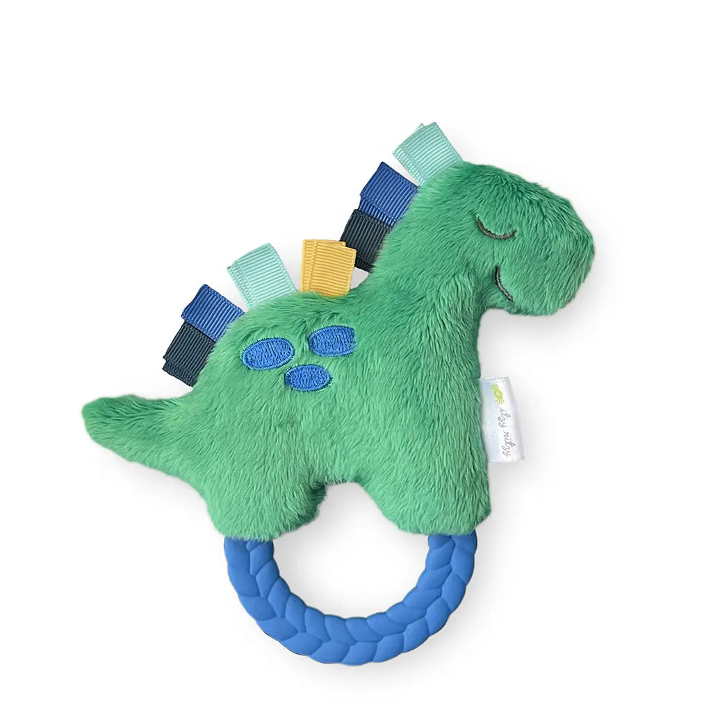 image of a rattle that is in the shape of a dinosaur that is green with three blue dots, a rubber blue teething ring, and light green, dark blue, yellow, fabric tabs as hair on a white background