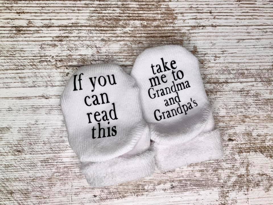 a picture of white baby socks that say if you can read this take me to grandma and grandpas sitting on top of a wood background