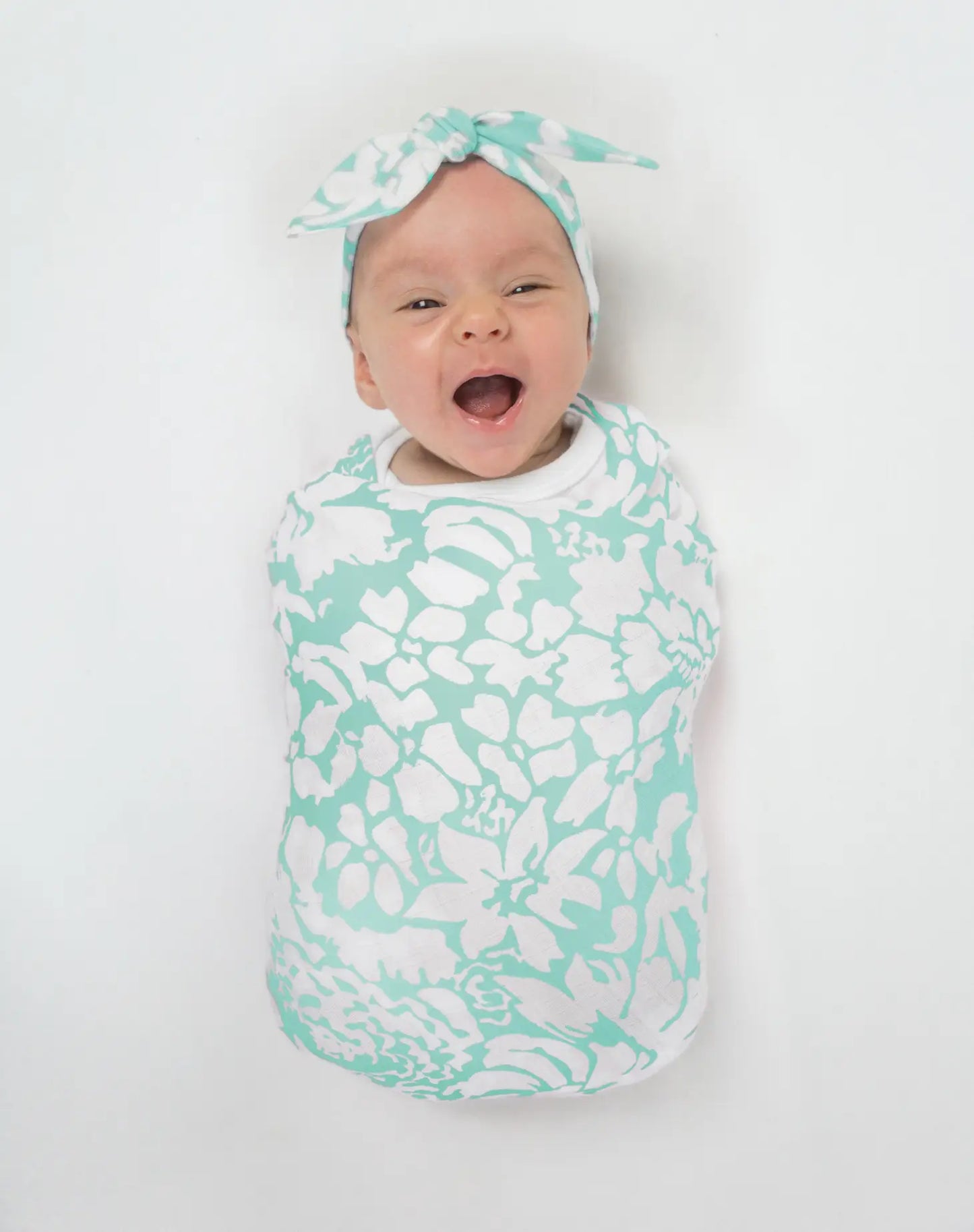 a picture of a white baby wrapped up in the swaddle smiling wearing a headband with the same pattern