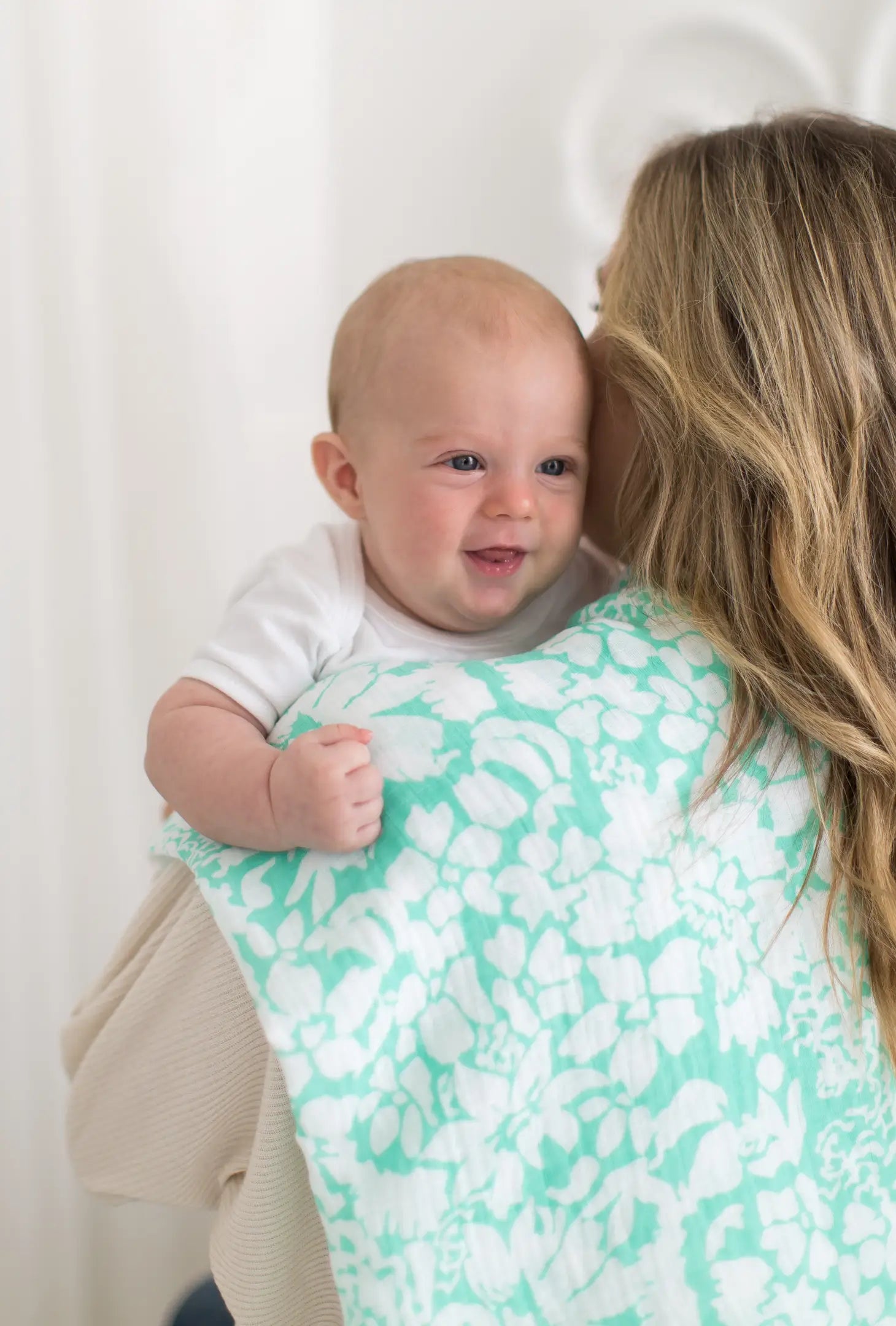 picture of a lady with blond hair with her back to the camera with a white baby looking over her shoulder and the swaddle on the ladys shoulder