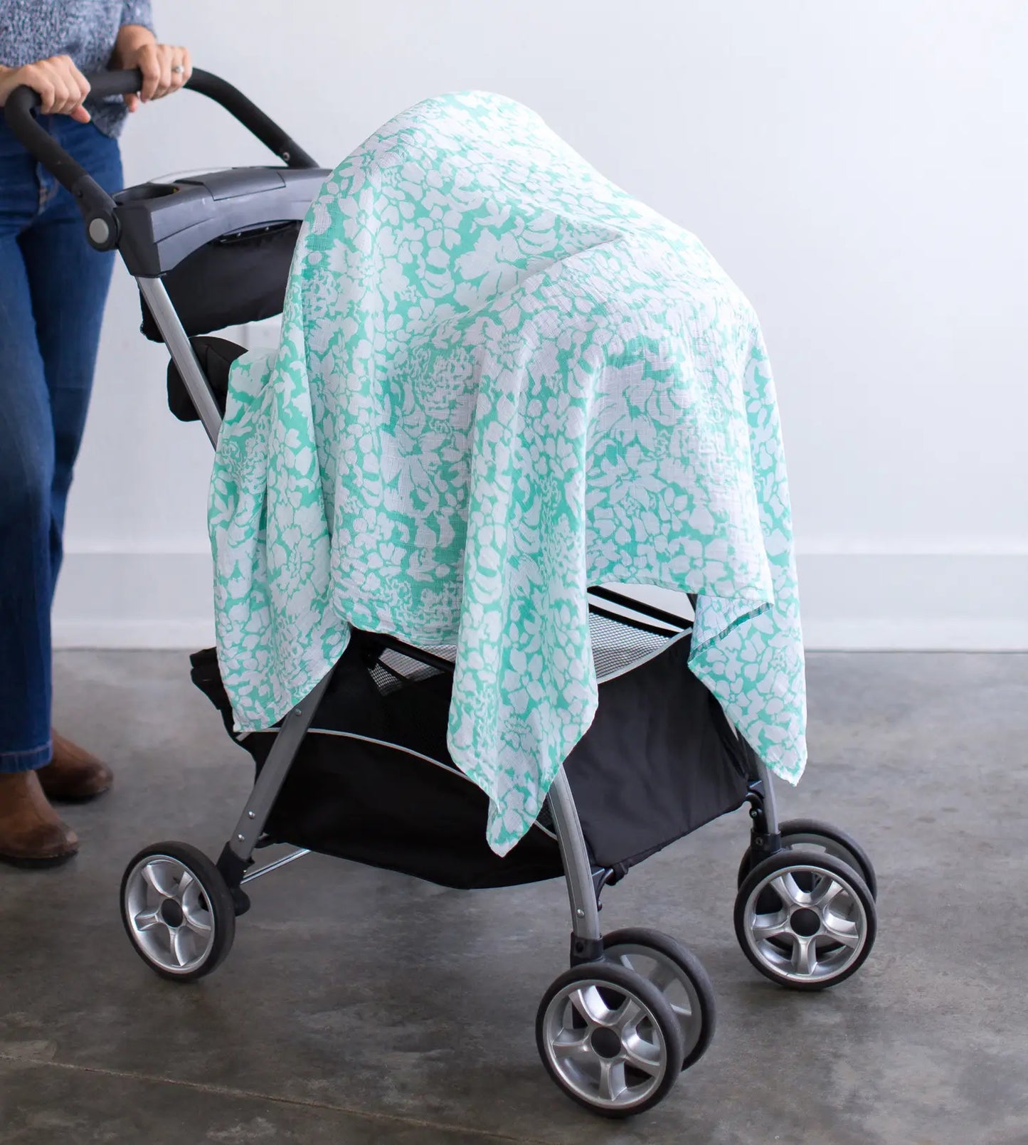 image of the swaddle draped over a stroller where a lady in jeans and flower shirt with brown boots is pushing it